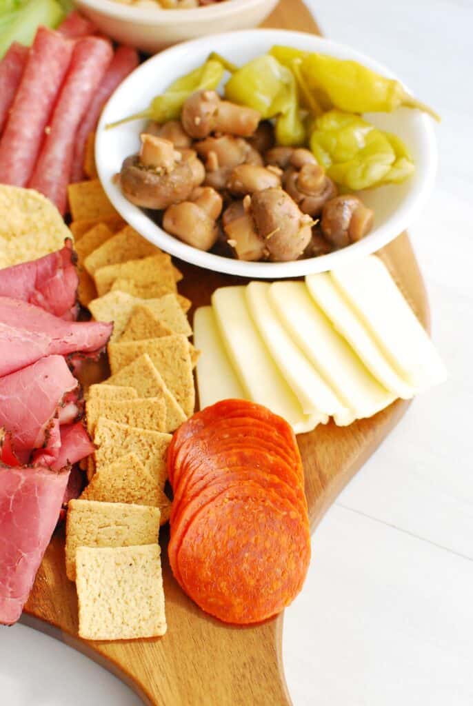 a close up showing keto crackers, pepperoni, cheese, and marinated mushrooms a close up showing keto crackers, pepperoni, cheese, and marinated mushrooms