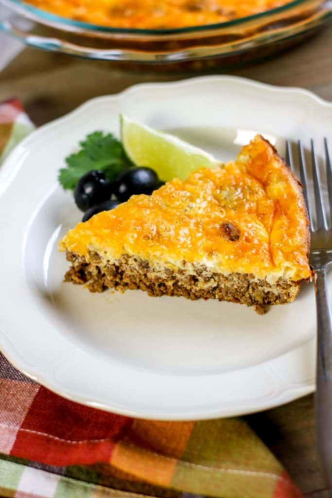 A slice of crustless taco pie on a white plate next to a few olives and a slice of lime A slice of crustless taco pie on a white plate next to a few olives and a slice of lime
