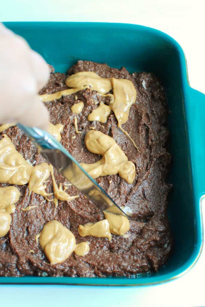a woman using a butter knife to swirl peanut butter into the brownie patter in a baking dish a woman using a butter knife to swirl peanut butter into the brownie patter in a baking dish