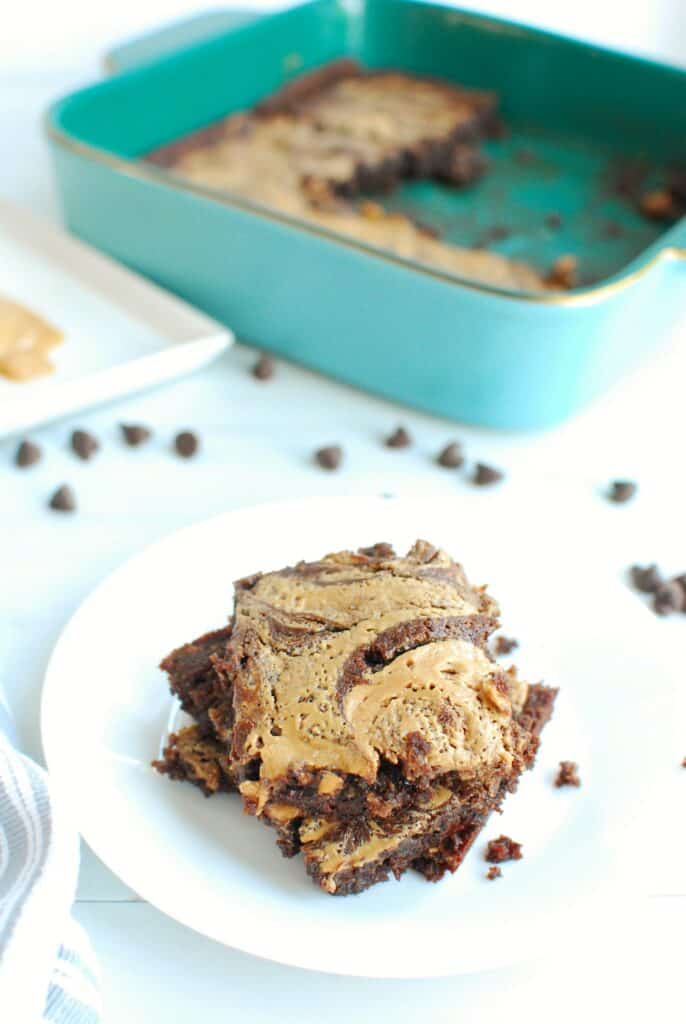 a stack of low carb peanut butter brownies focusing on the peanut butter swirl, placed on a white plate next to some scattered chocolate chips a stack of low carb peanut butter brownies focusing on the peanut butter swirl, placed on a white plate next to some scattered chocolate chips
