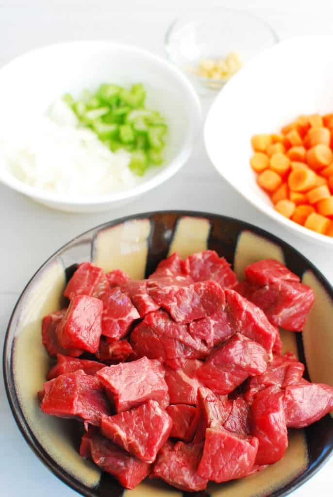 a bowl of beef stew meat, a bowl of carrots, and a bowl of onions and celery a bowl of beef stew meat, a bowl of carrots, and a bowl of onions and celery