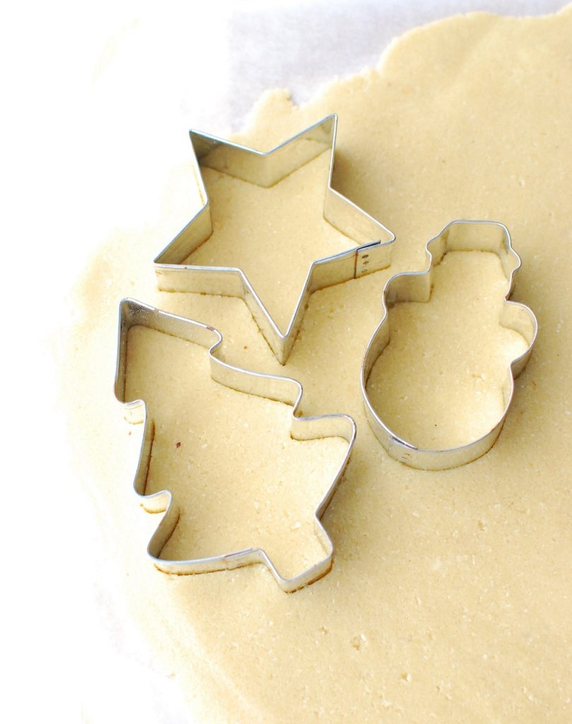 Several Christmas cookie cutters being used to make shapes out of cookie dough Several Christmas cookie cutters being used to make shapes out of cookie dough
