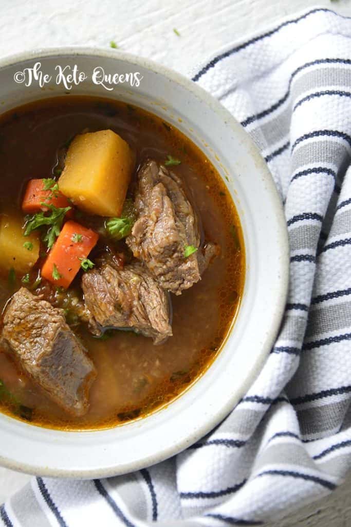 slow cooker keto beef stew in a white bowl next to a stripped towel slow cooker keto beef stew in a white bowl next to a stripped towel