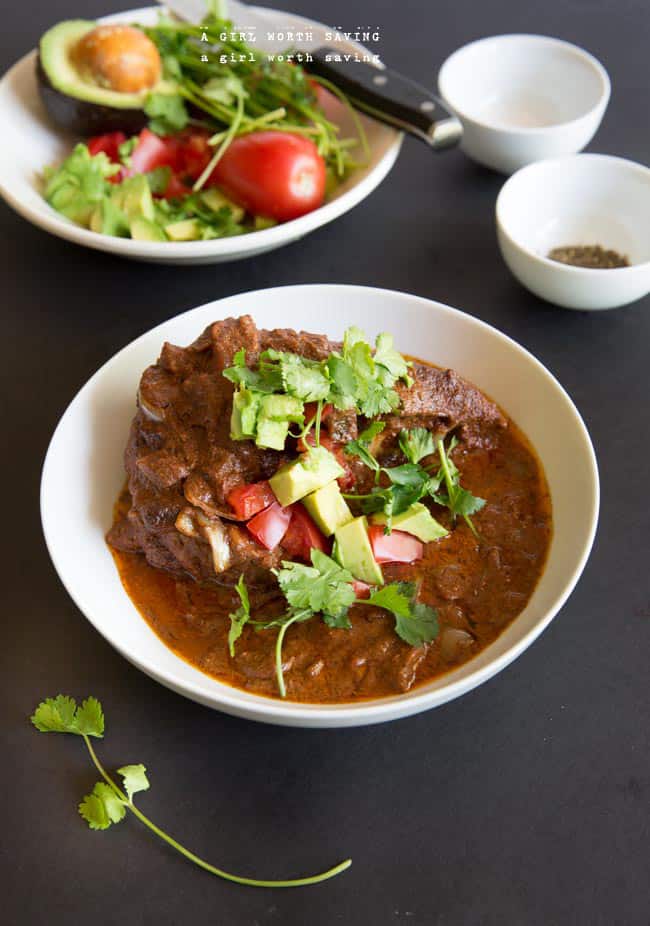 slow cooker keto chocolate chicken mole in a white bowl beside a salad slow cooker keto chocolate chicken mole in a white bowl beside a salad