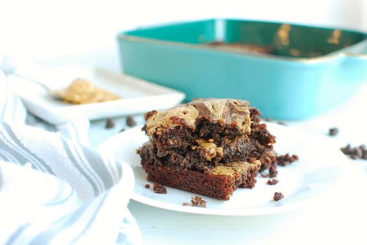 three fudgy keto peanut butter brownies on a white plate next to a napkin and the baking dish