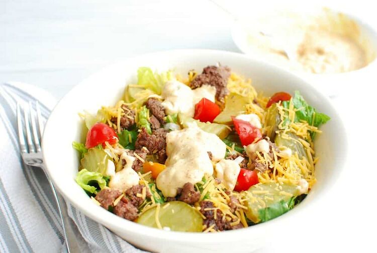 a bowl of keto big mac salad next to a napkin and a bowl of dressing
