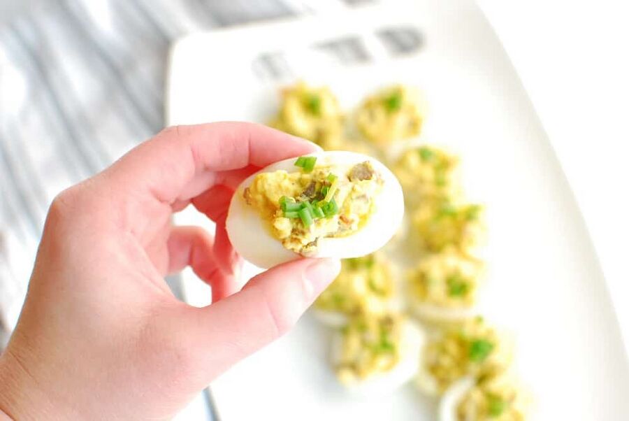 A woman's hand holding a low carb deviled egg with mushrooms and shallots A woman's hand holding a low carb deviled egg with mushrooms and shallots