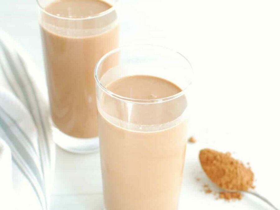 two tall glasses of keto chocolate milk next to a spoonful of cocoa powder two tall glasses of keto chocolate milk next to a spoonful of cocoa powder