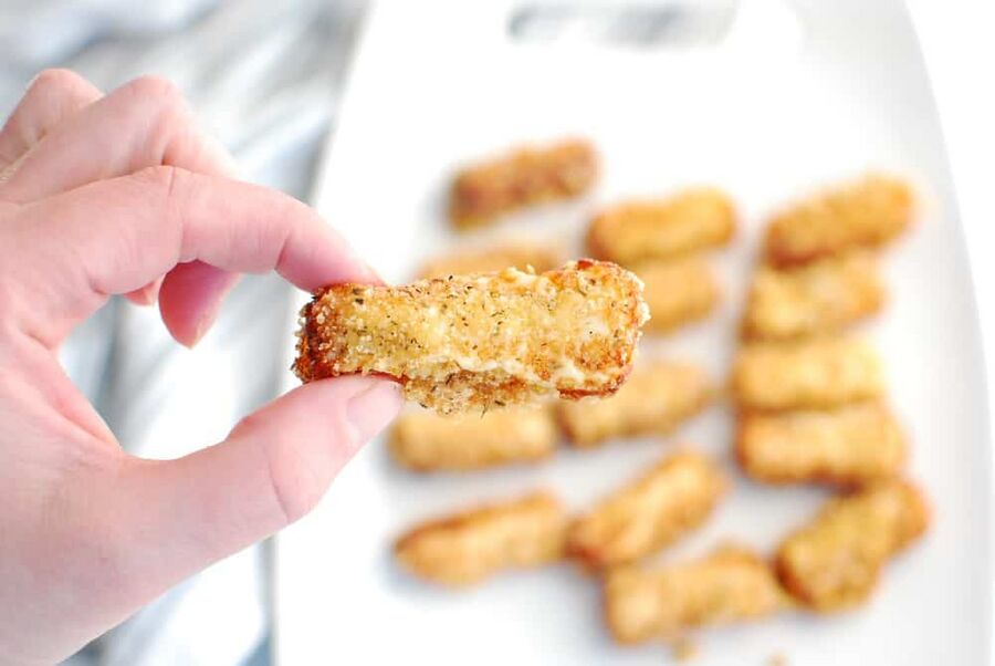 A woman's hand holding a low carb mozzarella stick A woman's hand holding a low carb mozzarella stick