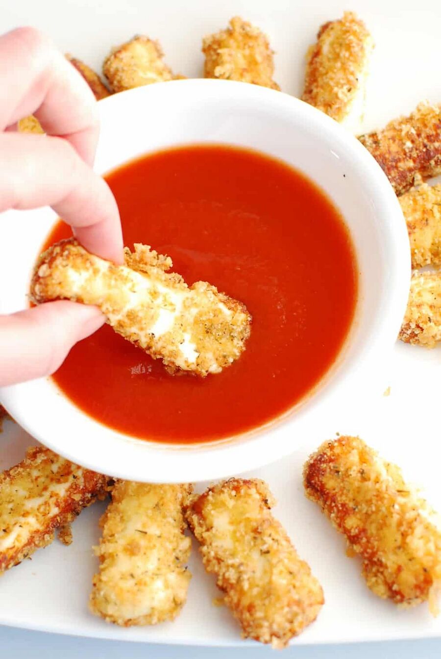 Dipping a keto mozzarella stick into marinara sauce Dipping a keto mozzarella stick into marinara sauce