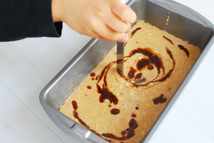a child's hand swirling together batter in a loaf pan a child's hand swirling together batter in a loaf pan