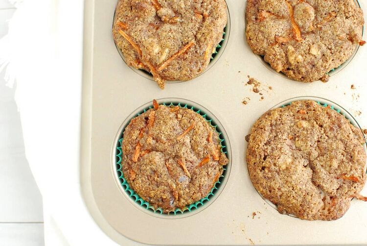 A close up of a muffin tin with a keto carrot cake muffin in a green paper liner.