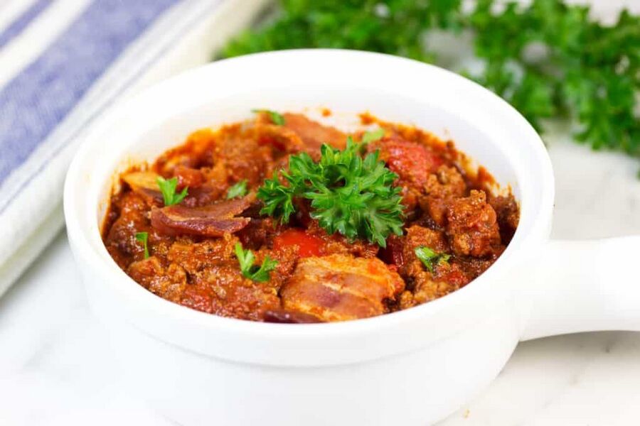 slow cooker keto beef chili with bacon in a white bowl topped with a green garnish slow cooker keto beef chili with bacon in a white bowl topped with a green garnish